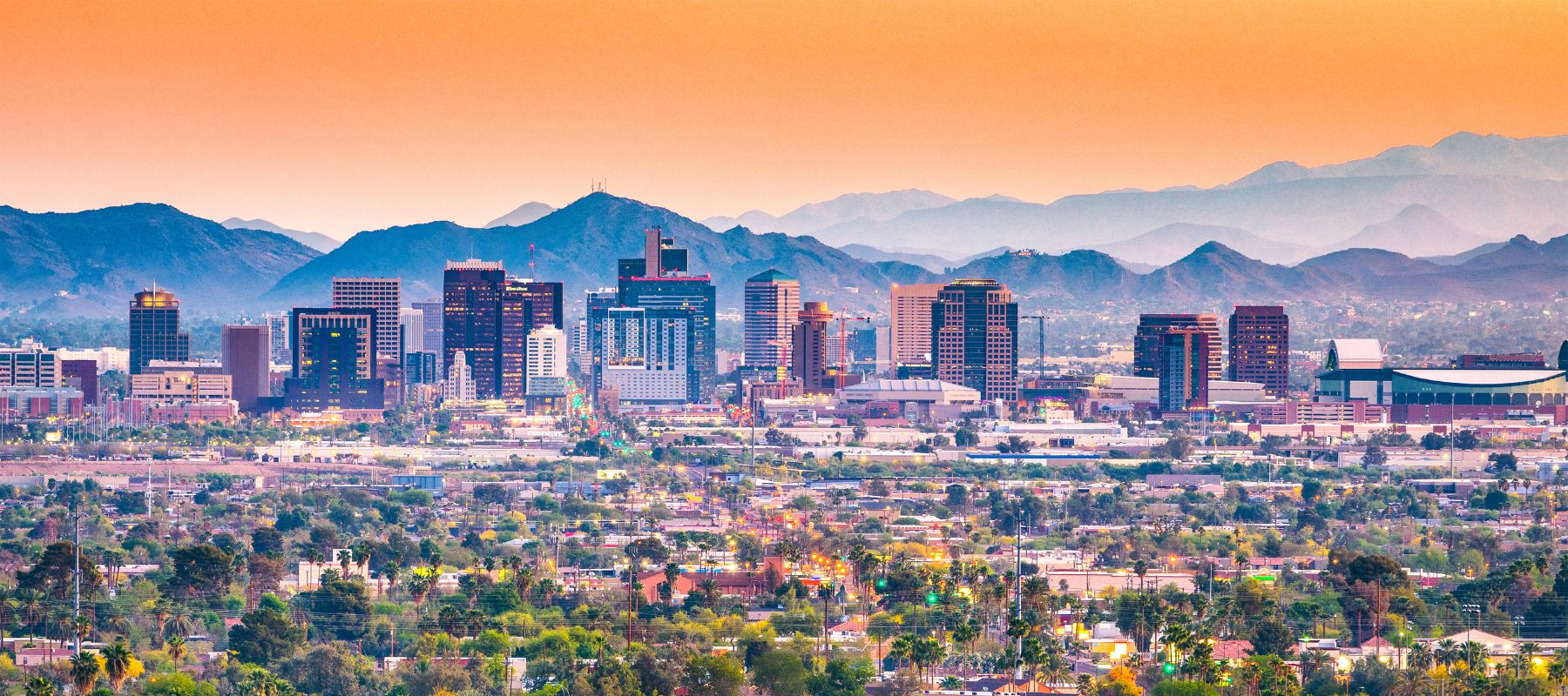 Phoenix, Arizona skyline at dusk with the city lights glowing against a backdrop of rugged desert mountains