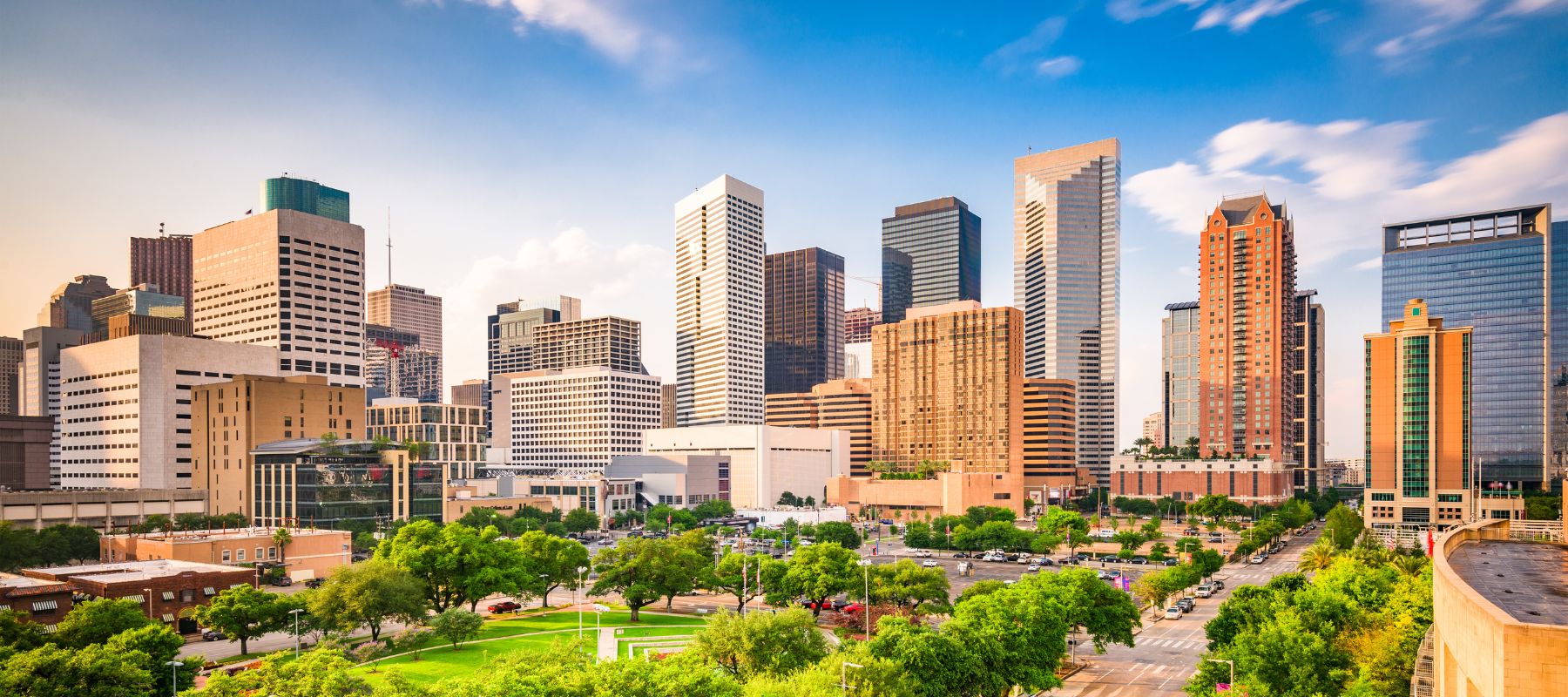 A wide view of the Houston, Texas skyline featuring modern skyscrapers and green park space in the foreground